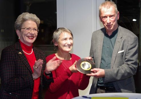 2 Frauen und 1 Mann stehen an einem Stehtisch. Die Frau in der Mitte und der Mann halten die Trophäe. Die Frau links klatscht Beifall.