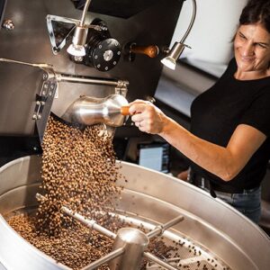 Frau röstet Kaffeebohnen in einer professionellen Kaffeeröstmaschine.