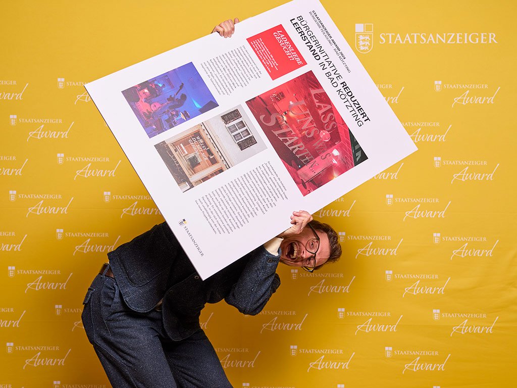 2. Platzierte der Kategorie Bürger:innenbeteiligung steht vor einer Pressewand und hält eine Projektcollage in die Kamera.