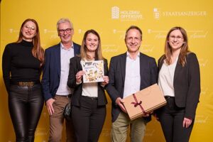 Eine Gruppe steht glücklich vor einer Pressewand und halten Urkunde und ein Geschenk in die Kamera.