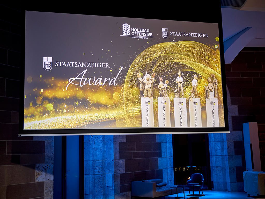 Bühne mit einer großen Leinwand, auf der „Staatsanzeiger Award“ und Trophäen vor einem funkelnden Hintergrund zu sehen sind.