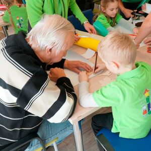 Ein älterer Herr und ein Kind sitzen an einem Tisch und basteln gemeinsam. Beide sind in das kreative Projekt vertieft.
