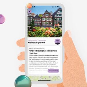 Eine Hand hält ein Smartphone, das Informationen über charmante Kleinstädte in Baden-Württemberg zeigt. Im Hintergrund sind bunte Fachwerkhäuser abgebildet.