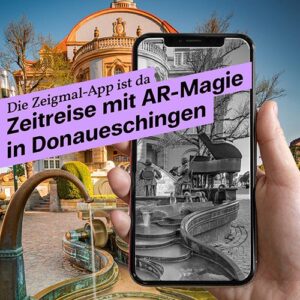 Ein Smartphone zeigt ein schwarz-weißes Bild eines historischen Brunnens, der mit der realen, farbigen Umgebung verschmilzt. Darüber steht: „Die Zeigmal-App ist da – Zeitreise mit AR-Magie in Donaueschingen.“