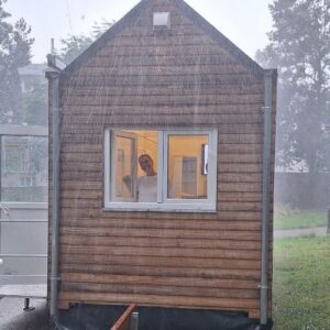 Außenansicht eines hölzernen Gartenhauses bzw. Schuppens mit geschlossenen Fenstern; im Hintergrund wirkt die Umgebung neblig oder bewölkt.