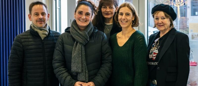 Gruppe von fünf Personen steht nebeneinander in einem Innenraum und lächelt in die Kamera, vermutlich bei einem gemeinsamen Termin oder Treffen in einem Büro- oder Veranstaltungsumfeld.