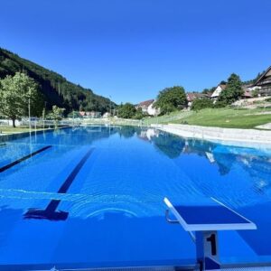 Startblock am Beckenrand des modernisierten Freibads Nordrach mit klarem Wasser und Bergkulisse im Hintergrund.