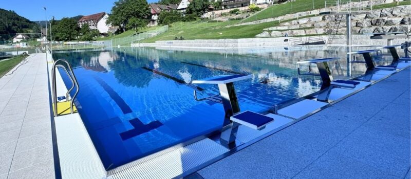 Schwimmerbecken im Freibad Nordrach mit Startblöcken und Blick auf die umliegenden Häuser und Natur.