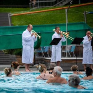 Bläserensemble im Bademantel spielt Konzert im Freibad vor Publikum im Wasser