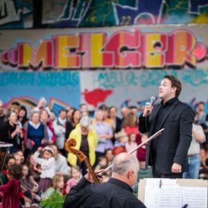 Dirigent spricht vor Publikum bei Konzert der Bodensee Philharmonie mit Graffiti-Hintergrund