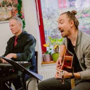 Sänger mit Gitarre und Pianist geben ein intimes Konzert in einer Einrichtung