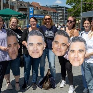 Gruppe von Fans hält große Masken eines Musikstars in der Gelsenkirchener Innenstadt