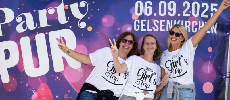 Drei Frauen posieren gut gelaunt vor einer Eventwand beim Fan-Event in Gelsenkirchen