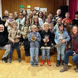 Kindergruppe mit Trompeten und anderen Blasinstrumenten steht auf einer Bühne in einem Proberaum
