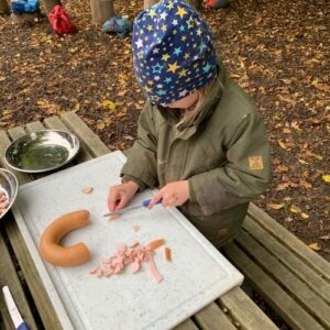 Kind schneidet Wurst beim gemeinsamen Kochen im Freien