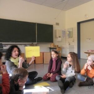 Musikpädagogin arbeitet mit Kindern im Sitzkreis und erklärt rhythmische Übungen