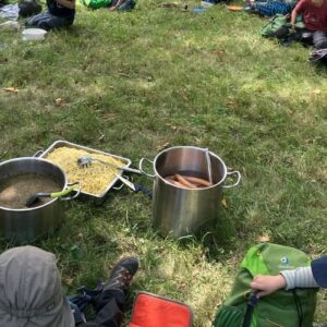 Gemeinsames Kochen im Freien mit Töpfen und Lebensmitteln auf einer Wiese