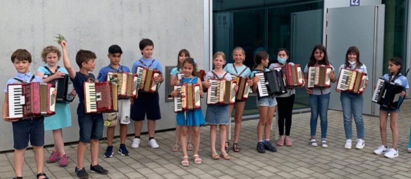 Kindergruppe steht mit Akkordeons vor einem Gebäude und präsentiert ihre Instrumente