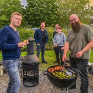 Teilnehmende stehen gemeinsam am Grill und essen in lockerer Atmosphäre