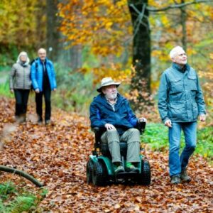 Senior fährt mit elektrischem Rollstuhl auf einem befestigten Wanderweg im Wald