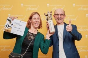 Zwei Personen präsentieren Urkunde und Trophäe des Staatsanzeiger Awards 2025 und freuen sich über den ersten Platz für das Projekt der Stadt Pforzheim.