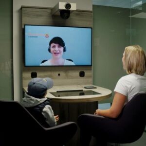 Digitale Beratungssituation: Mutter und Kind sitzen vor Bildschirm und sprechen mit Verwaltungsmitarbeiterin per Video